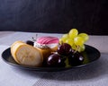 A black plate with cherries, grapes, a banana, a cupcake lies on a table in the background