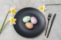 Black plate with Easter eggs, yellow daffodil flowers and cutlery on textured gray background. Top view, flat lay Royalty Free Stock Photo