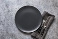 Black plate, fork and knife on grey stone table. Minimal table place setting. Space for text or menu. View from above Royalty Free Stock Photo