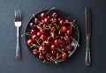 Black plate with fresh sweet cherry and cutlery on dark stone background. Royalty Free Stock Photo