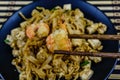 Black plate with pad thai on a bamboo mat. Chopsticks with shrimp