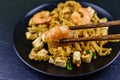 Black plate with pad thai on a slate board. Chopsticks with shrimp