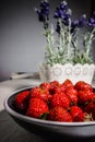 Black plate with juicy strawberry, front view. Fresh red berries in a black plate on a white table on the background of pots with Royalty Free Stock Photo