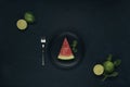 Black plate with slice of watermelon, fork, mint and lime on dark textured background Royalty Free Stock Photo