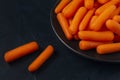 Black plate with small peeled pieces of carrot on dark textured backdrop