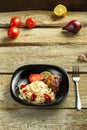 Black plate of spaghetti with baked chicken with a fork on a wooden table near vegetables. Royalty Free Stock Photo