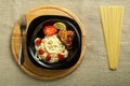 Black plate of spaghetti with baked chicken on a stand with a fork next to uncooked pasta. Royalty Free Stock Photo