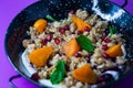 Black plate of sweet breakfast of bulgur porridge with pomegranate, peach and fruits with mint.