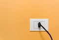 Black Plug in a Wall Socket on an Orange Wall Royalty Free Stock Photo