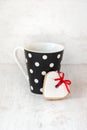 Black polka dotted coffee cup with a heart shaped homemade cookie over white wood background. Royalty Free Stock Photo