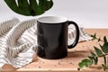 Black porcelain mug on wooden desktop next to striped tablecloth, scattered crystals and green twigs against white
