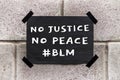 Black poster on gray brick wall. Banner with text No Justice No Peace, tag Black Lives Matter. Anti-racism