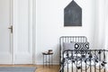 Black poster on white wall above bed in simple bedroom interior with door and table