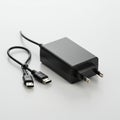 A black power adapter with two flat prongs is positioned on a light surface. Attached Royalty Free Stock Photo