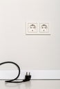 Black power cord cable unplugged with european wall outlet on white plaster wall Royalty Free Stock Photo