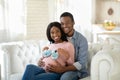 Black pregnant woman with tiny baby boties and her happy husband hugging on sofa at home Royalty Free Stock Photo