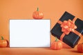 Black present box with orange ribbon and pumpkin and empty blank lightbox on orange background. Happy halloween