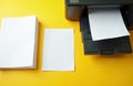 Black printer sits on bright yellow background alongside blank paper sheets. Workspace setup displays modern office equipment Royalty Free Stock Photo