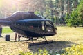 Black private modern luxury helicopter standing on grass field near forest at country rural landscape. Rich buiness lifestyle