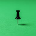 A black pushpin is inserted into a bright green surface. The pushpin has a standard Royalty Free Stock Photo