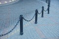 Black railing from iron chains and pillars on a gray pavement of stones Royalty Free Stock Photo