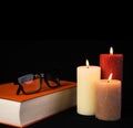 Black Readig Glasses on orange book with three burning candles Royalty Free Stock Photo