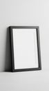 A black rectangular picture frame leans against a white wall on a flat surface. The Royalty Free Stock Photo