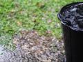 Black recycling plastic bucket on the floor outdoor surrounding with green area environment, raindrops splash and reflection o