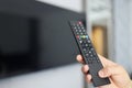 Black remote control in hand in front of TV Royalty Free Stock Photo