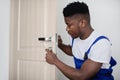 Black Repairman Installing And Fixing Lock On Front Door Indoors