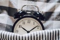 Black retro alarm clock sleeping on pillow with blanket metaphor of insomnia, late at work, well sleep with time countdown or wake