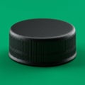 A black, ribbed plastic bottle cap is set against a solid green background. The cap\'s Royalty Free Stock Photo