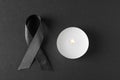 Black ribbon and burning candle on dark background. Funeral symbols