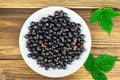 Black ripe currant in plate on wooden background, top view