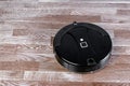 Black robotic vacuum cleaner runs on laminate floor. Robot controlled by voice commands for direct cleaning. Modern smart