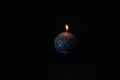 Black, round candle with texture burning isolated on black background.