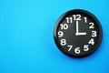 Black round clock showing five o`clock on blue background Royalty Free Stock Photo