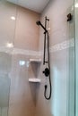 Black round shower head on tile wall of shower stall with hinged glass door