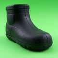 A black rubber ankle boot is placed against a bright green background. The boot has a Royalty Free Stock Photo