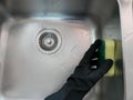 Black rubber gloved hand holding a sponge and cleaning a stainless steel sink