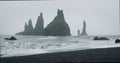 The black sand beach of Reynisfjara with waves hitting the shore on foggy rainy stormy day Vik, Iceland