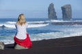 Beautiful blonde woman sits on beach stone, near to the iconic wild rock formations next to Mosteiros, in Sao Miguel island, Azore Royalty Free Stock Photo