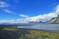 Black sand beach with vegetation and clouds sticking to mountain range