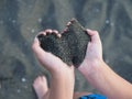 Black sand in children`s hands in the form of a heart Royalty Free Stock Photo