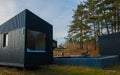Black Scandinavian-style modular house with a terrace, wooden terrace chairs among coniferous forest