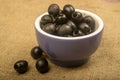 Black seedless olives in a ceramic bowl and a few scattered olives on a background of coarse-textured fabric. Close up Royalty Free Stock Photo