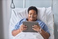 Black senior woman holding digital tablet while laying on bed in hospital Royalty Free Stock Photo