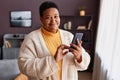 Black senior woman holding smartphone standing by window Royalty Free Stock Photo