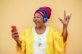 Black senior woman on traditional african dress dancing to rock music on mobile phone - Focus on face Royalty Free Stock Photo