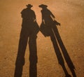 Black shadow of couple on yellow sand, silhouette of young traveling woman and man in hats with photo camera and bags